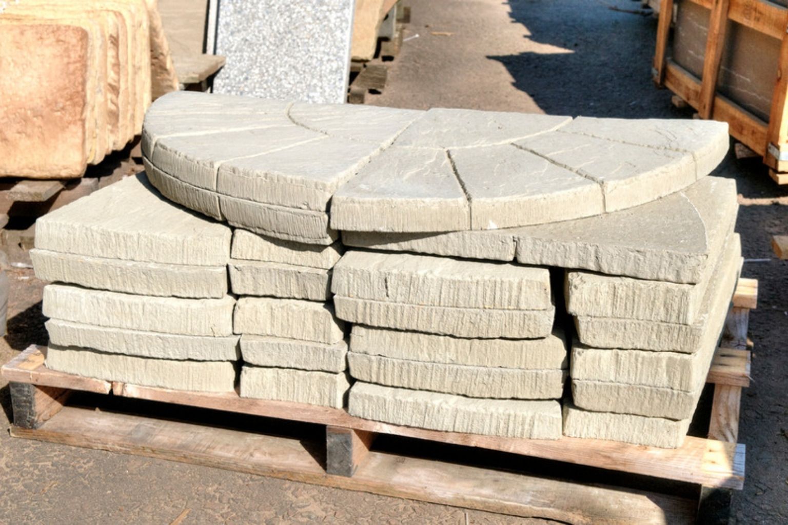 Betonfliser og buede kantfliser stablet på en palle klar til lægning